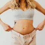 Mulher medindo a cintura com fita métrica, simbolizando o acompanhamento do progresso na perda de peso